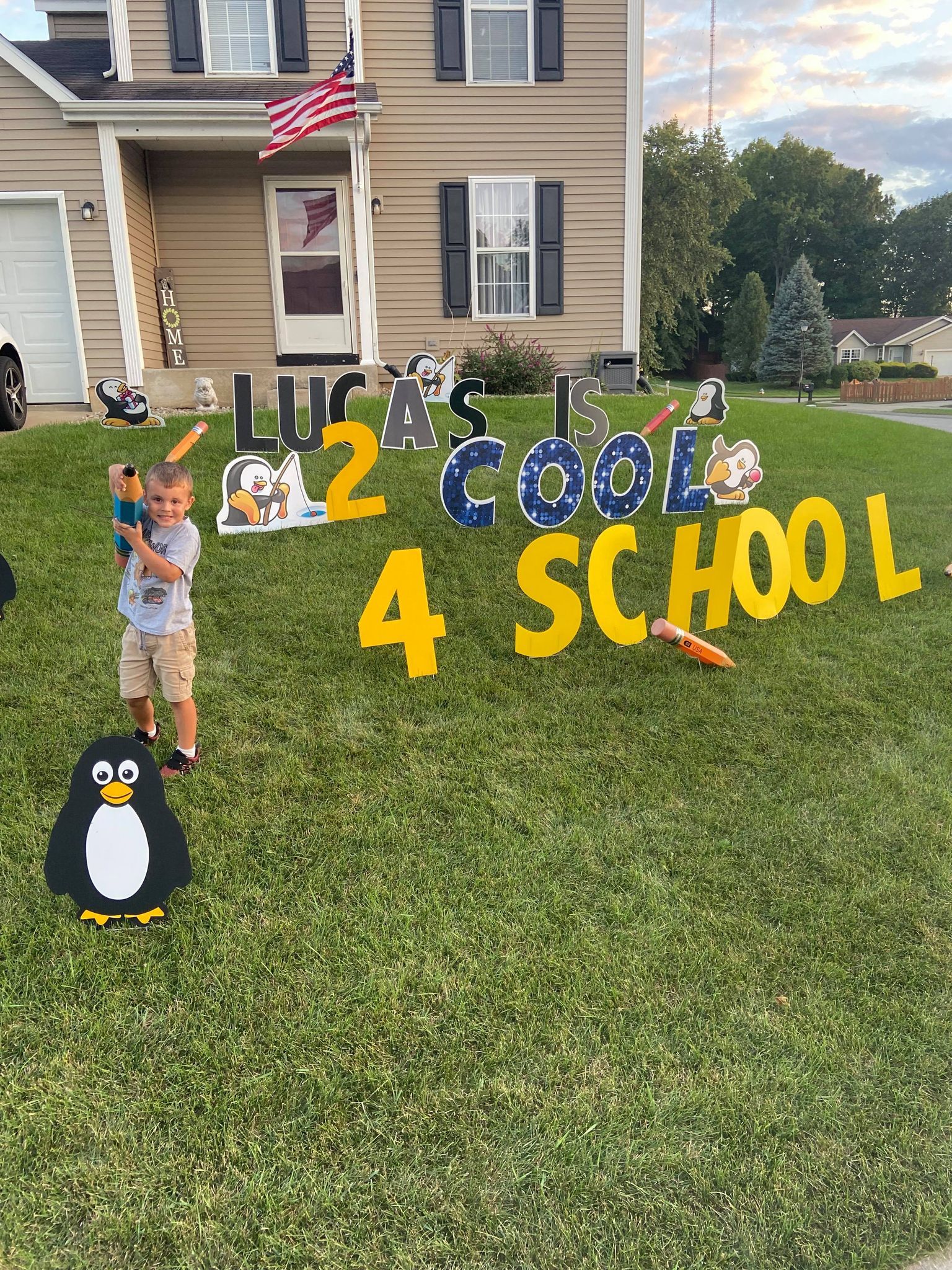 A woman is standing in front of a happy birthday sign in front of a house with penguin accents.