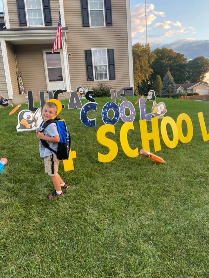 A young boy is standing in front of a sign that says school. Back to school themed yard card.