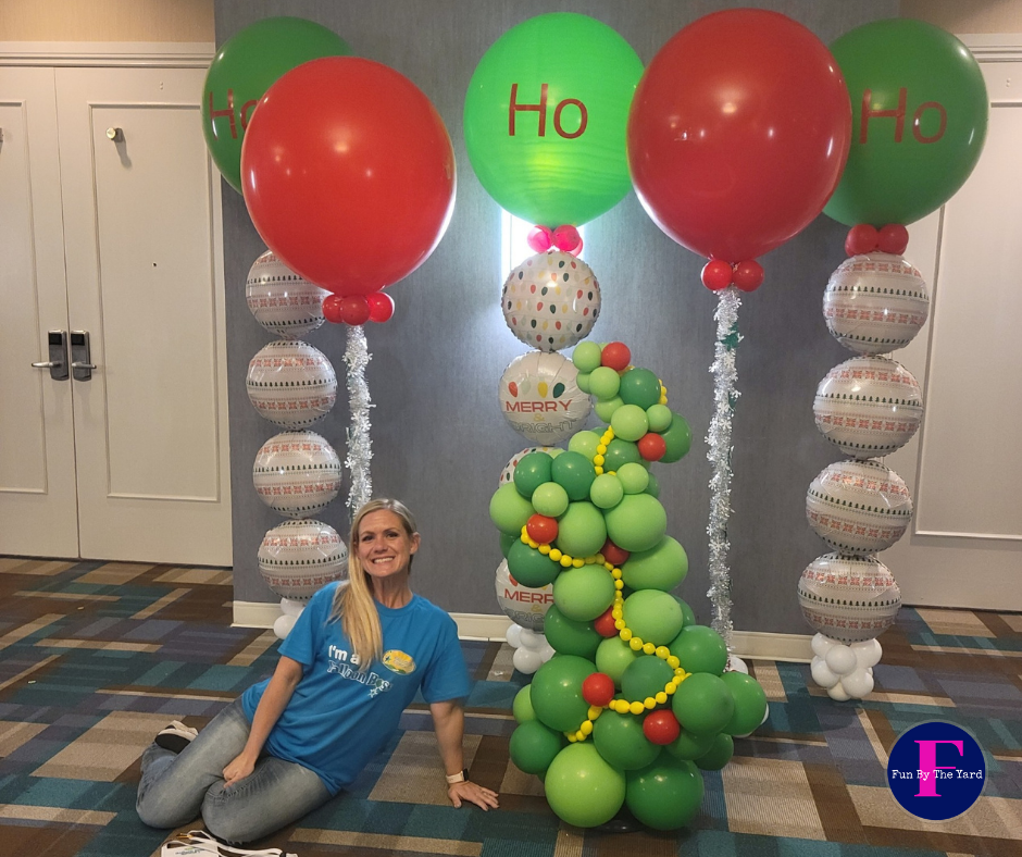 A woman is kneeling in front of a christmas tree made of balloons