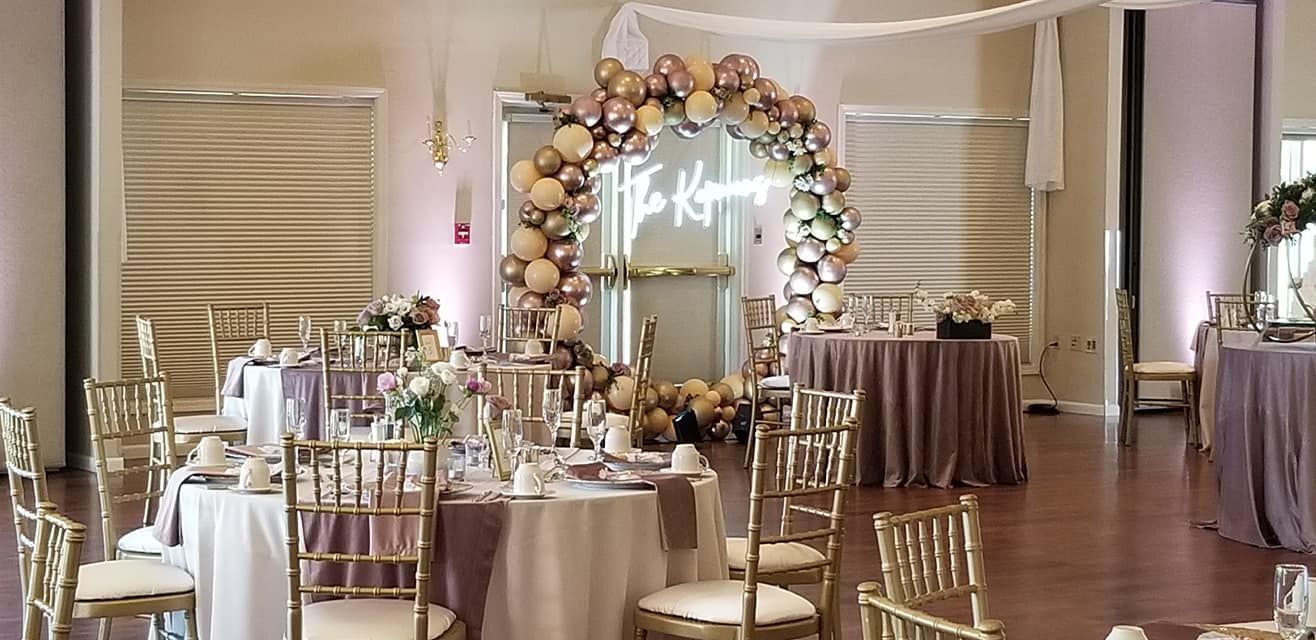 A large room with tables and chairs set up for a wedding reception. Balloon photo op