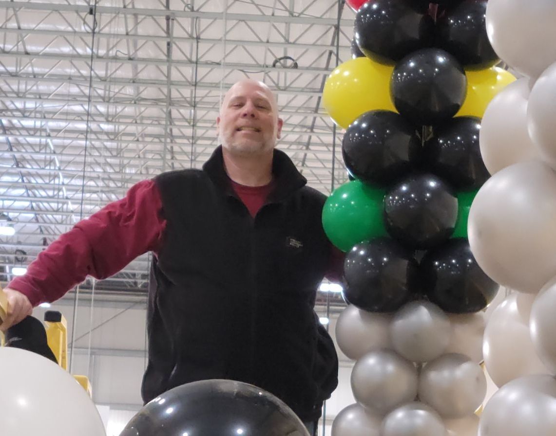 A man is standing in front of a bunch of balloons