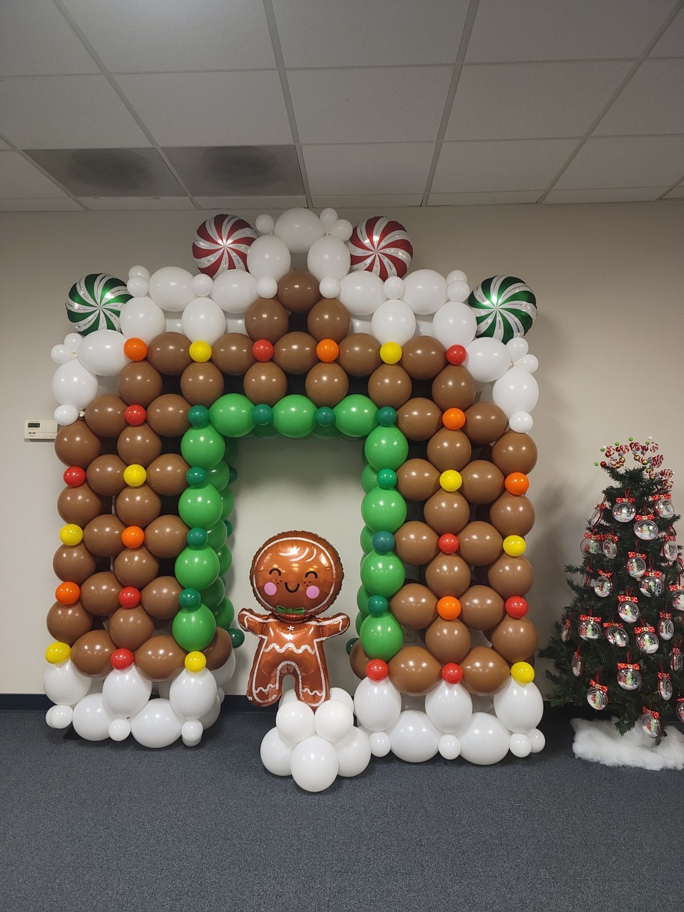A gingerbread man is standing in front of a gingerbread house made of balloons.