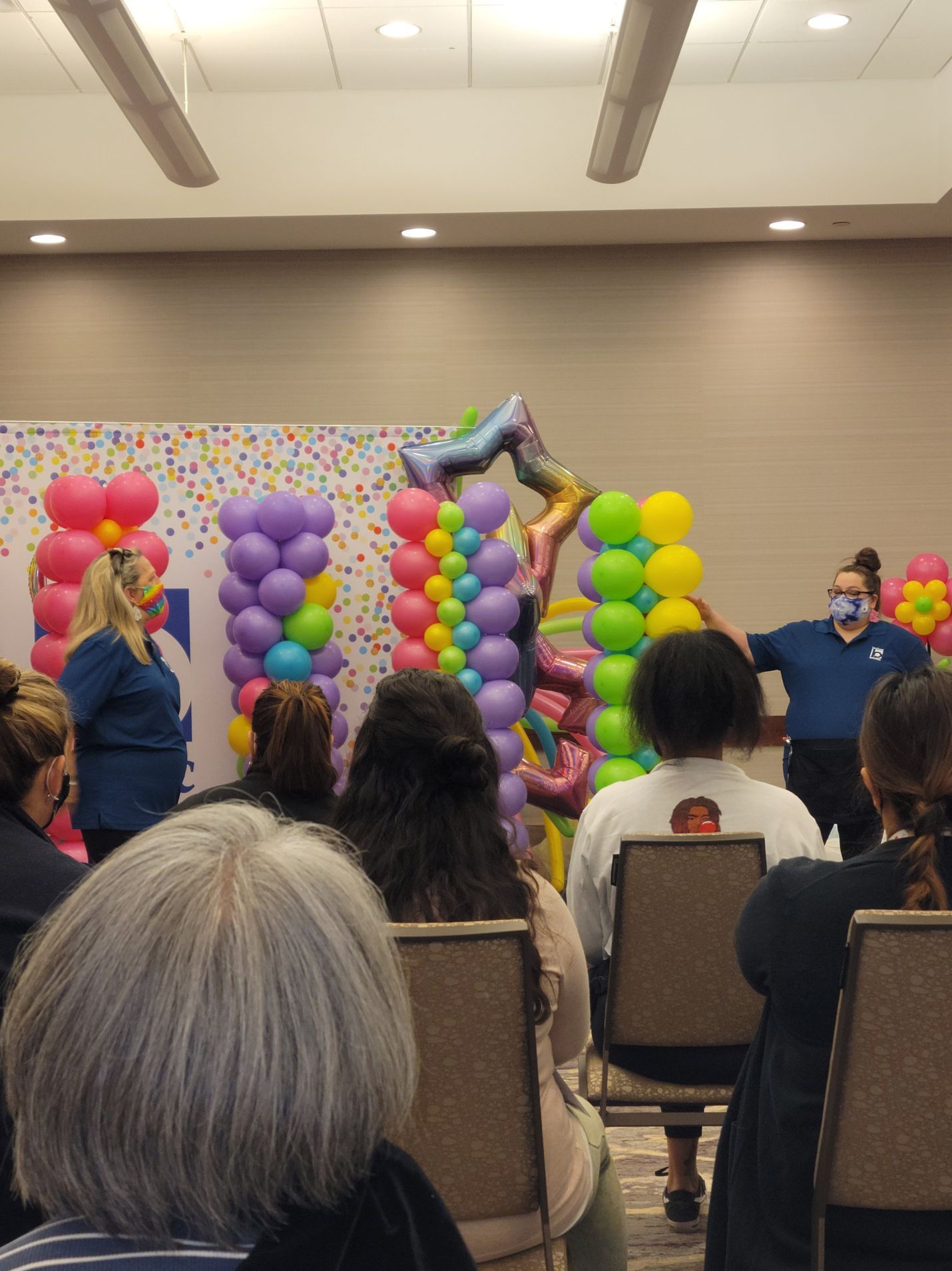 A group of people are sitting in chairs in front of balloons