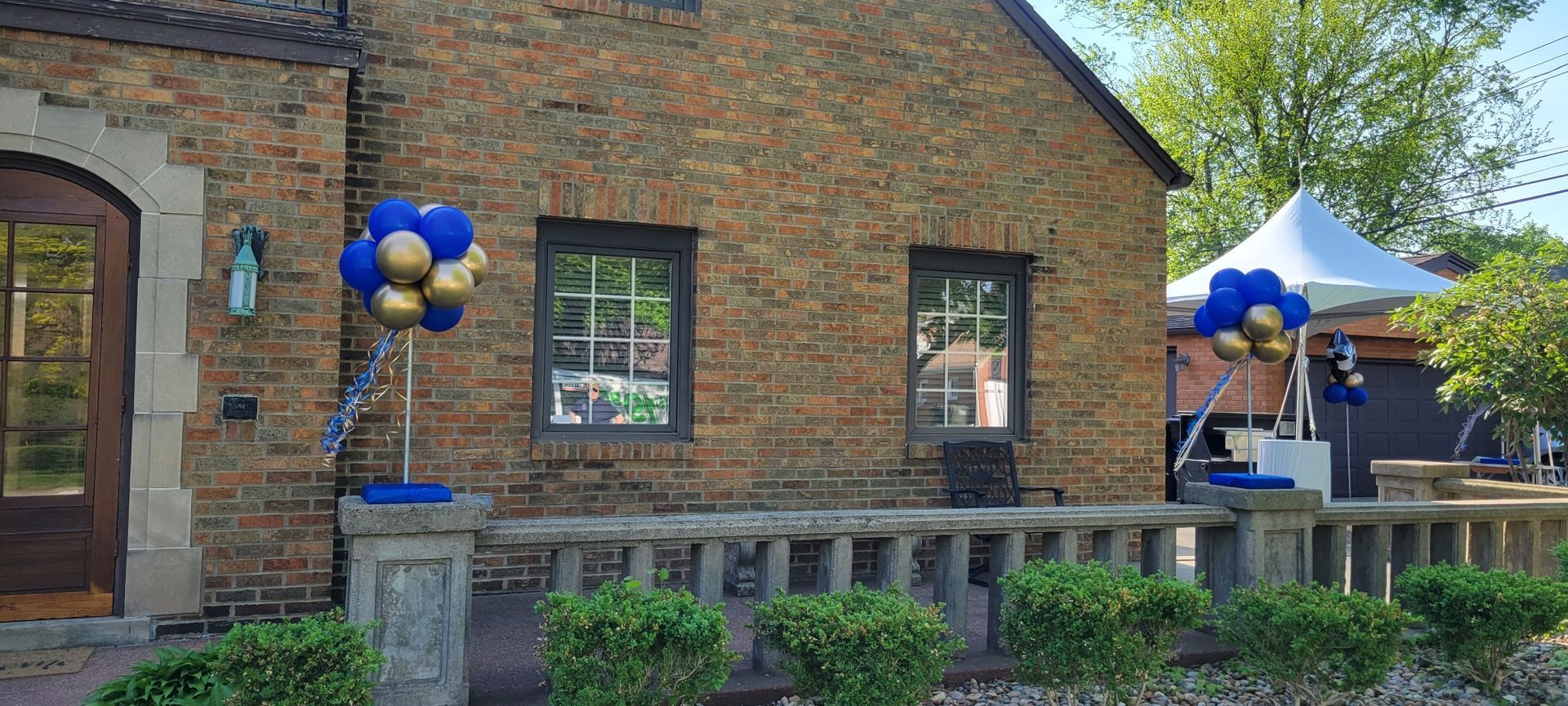 A brick house with blue and gold balloons in front of it.