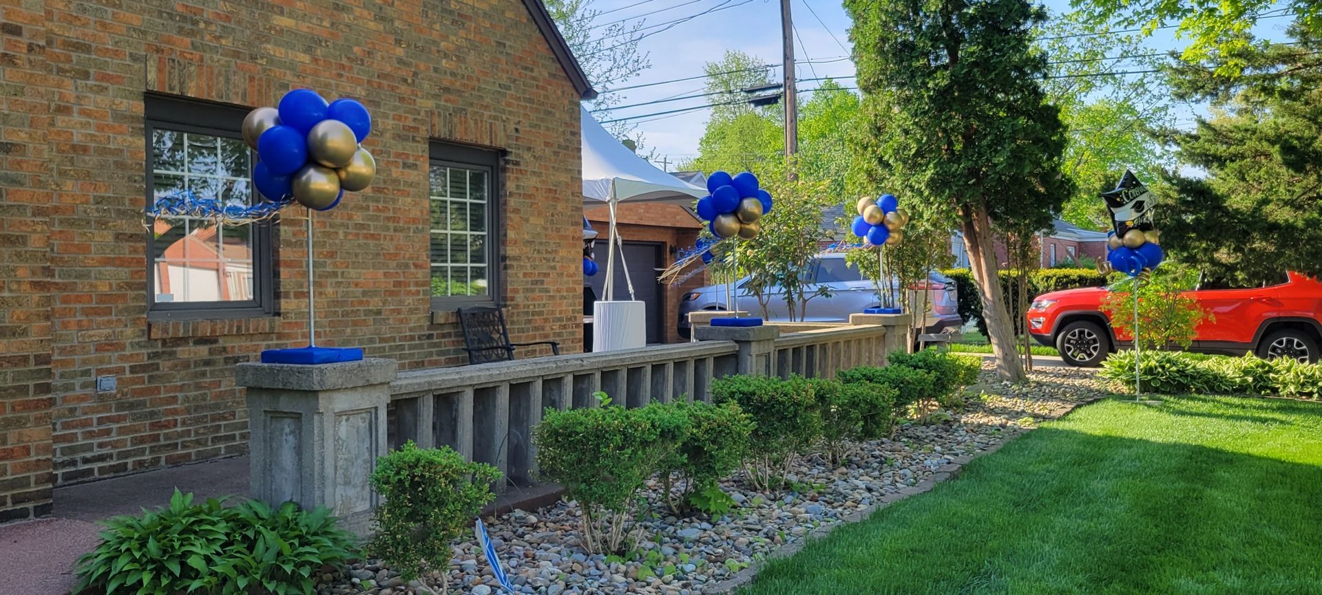 A brick house with blue and gold balloons in front of it.