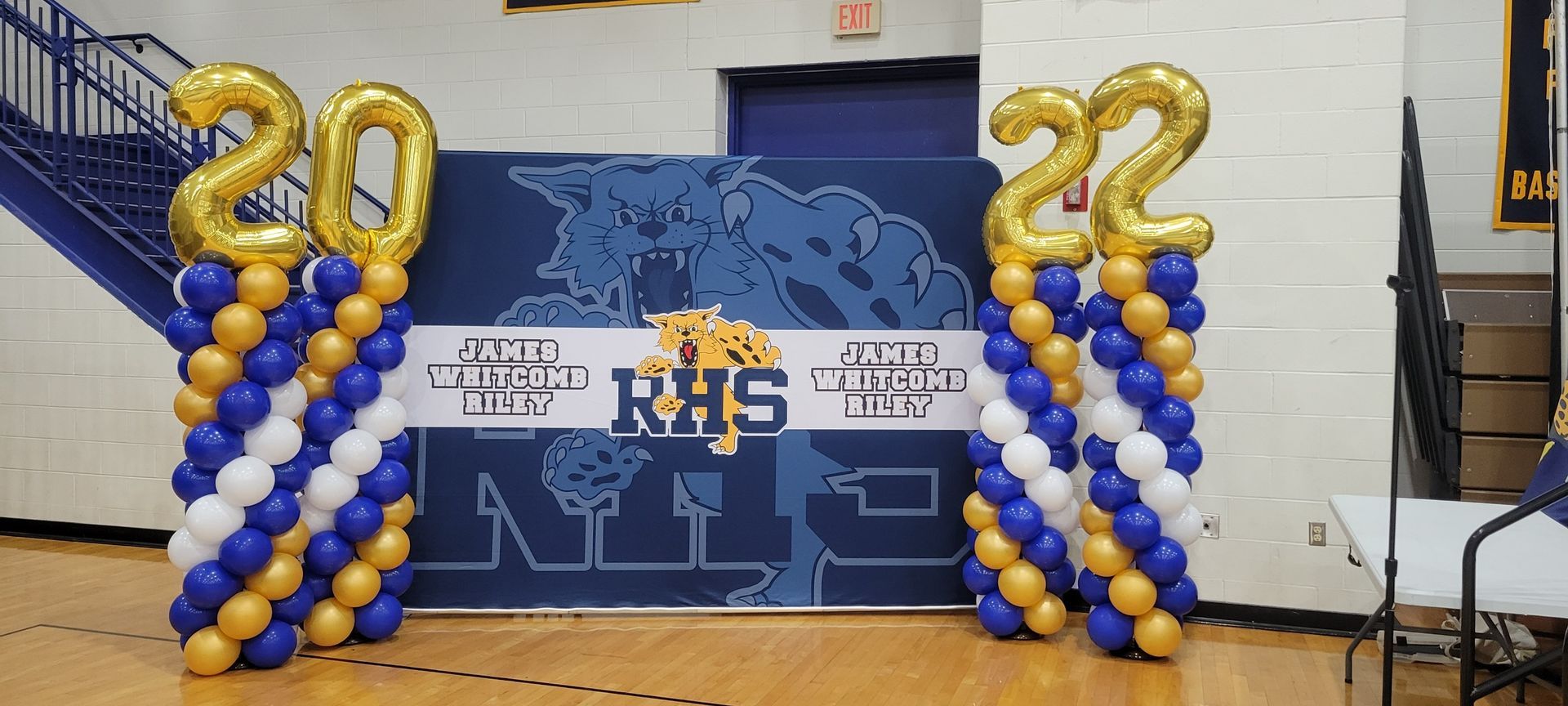 A basketball court decorated with blue and gold balloons for a graduation ceremony.