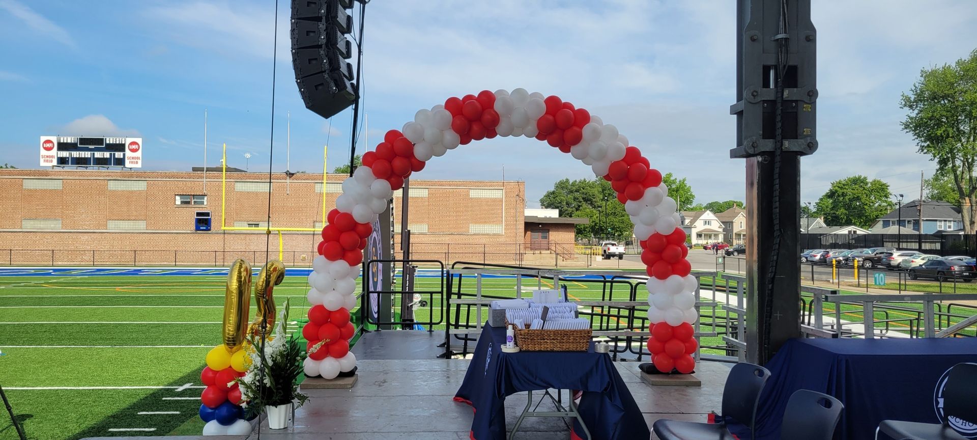 A stage decorated with red , white and blue balloons in front of a football field.