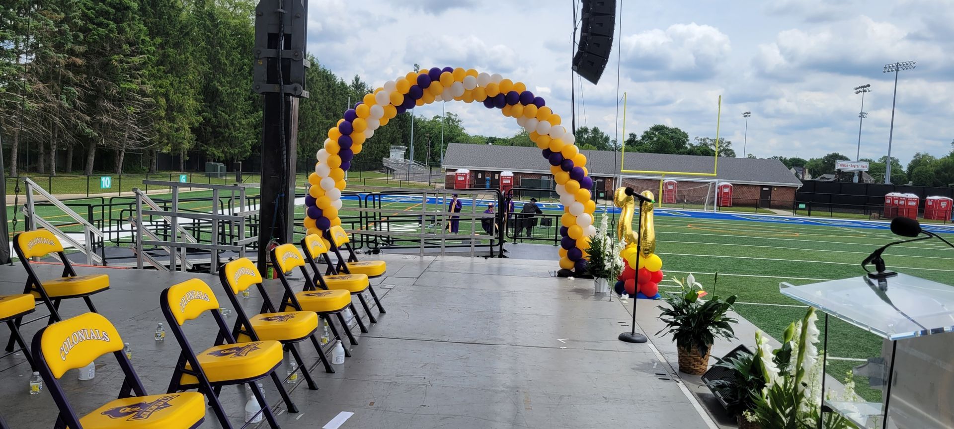 A stage with chairs and balloons on it in front of a football field.