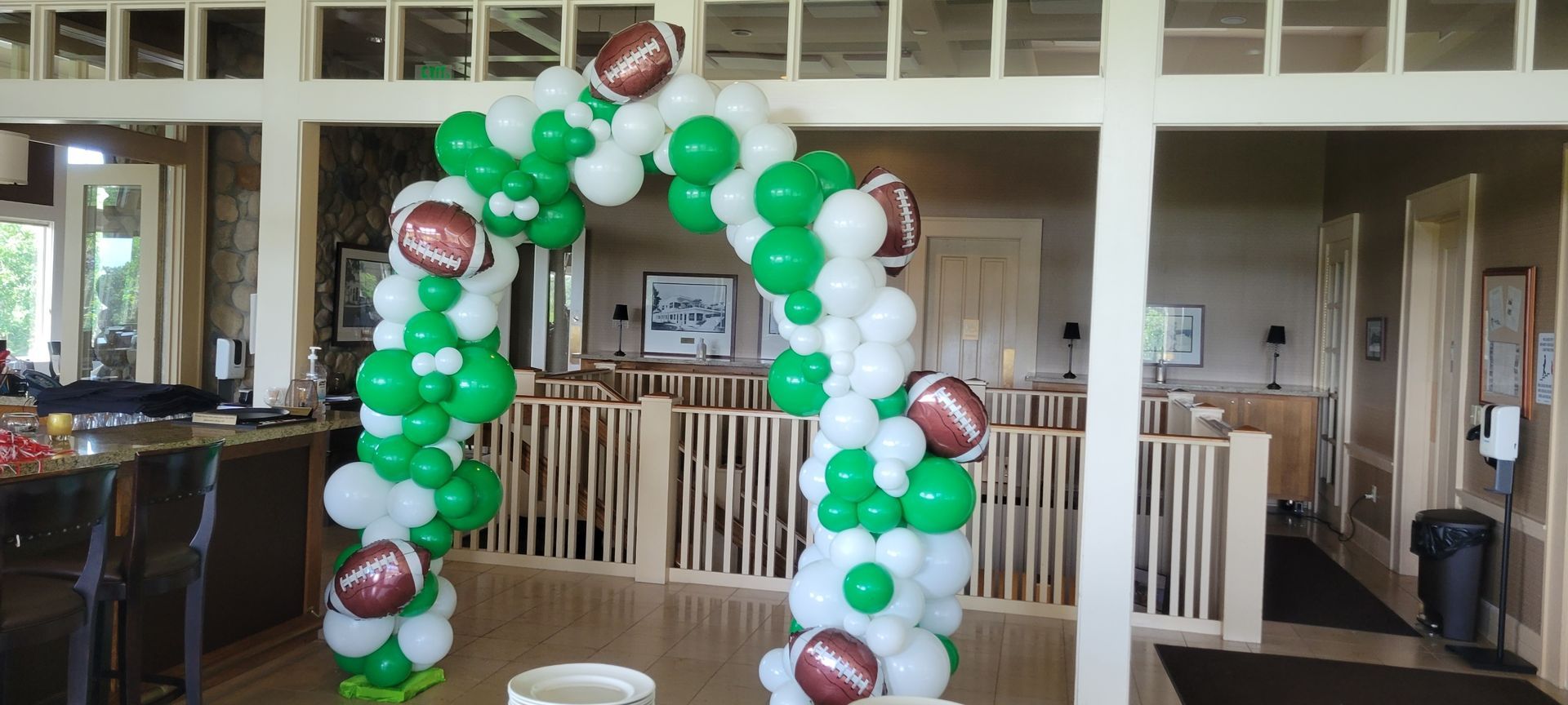 A room decorated with green and white balloons and footballs.