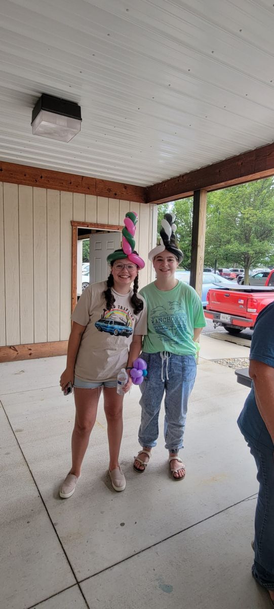 Two people wearing balloon hats are standing next to each other on a porch.