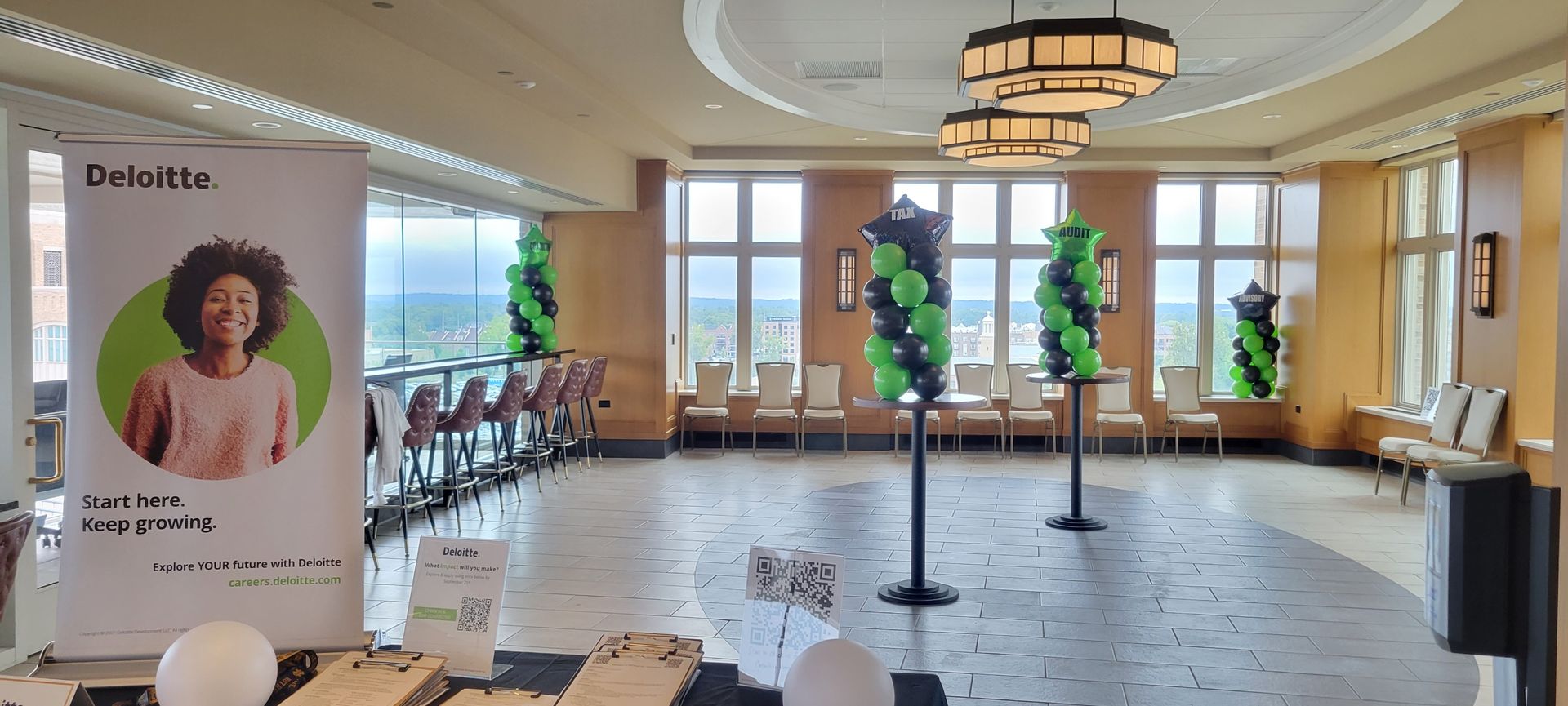 A banquet hall with balloon decorations, a banner, chairs, and large windows with a view.