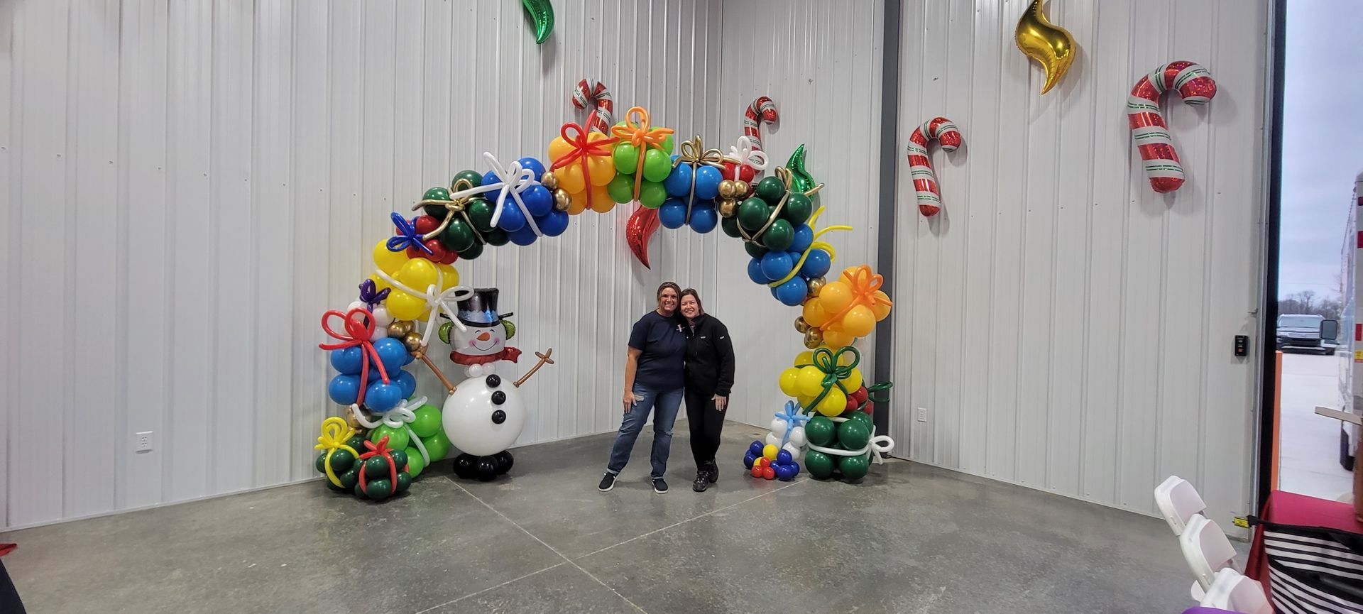 A couple of people standing in front of a balloon arch.