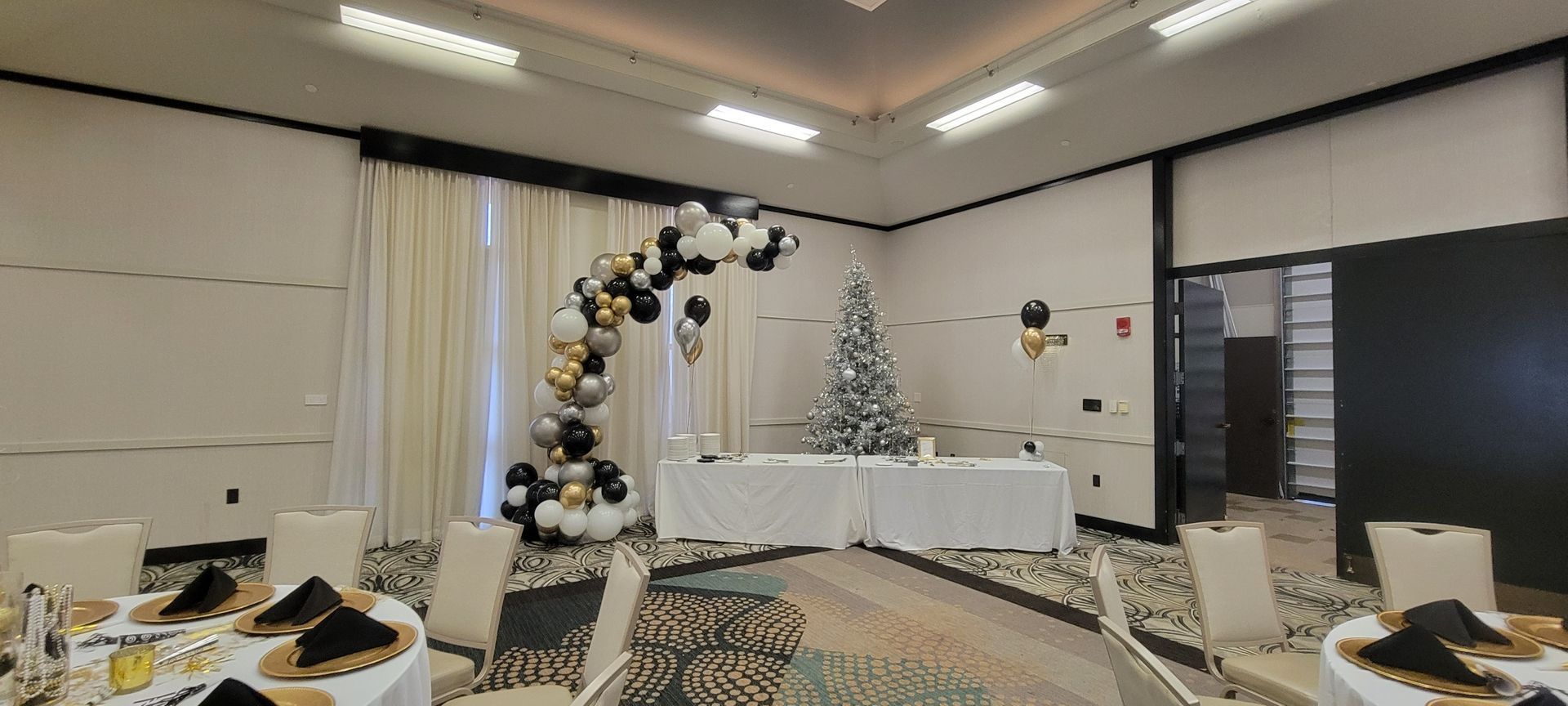A large room with tables and chairs and a christmas tree. Balloon demi arch