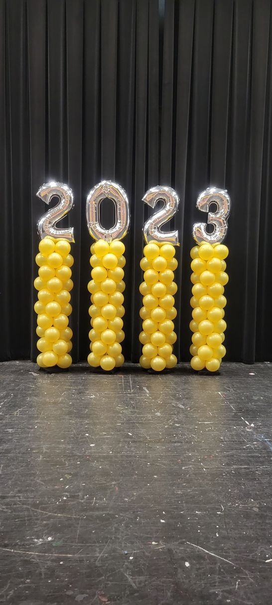 A row of yellow balloons shaped like the year 2023 on a stage.