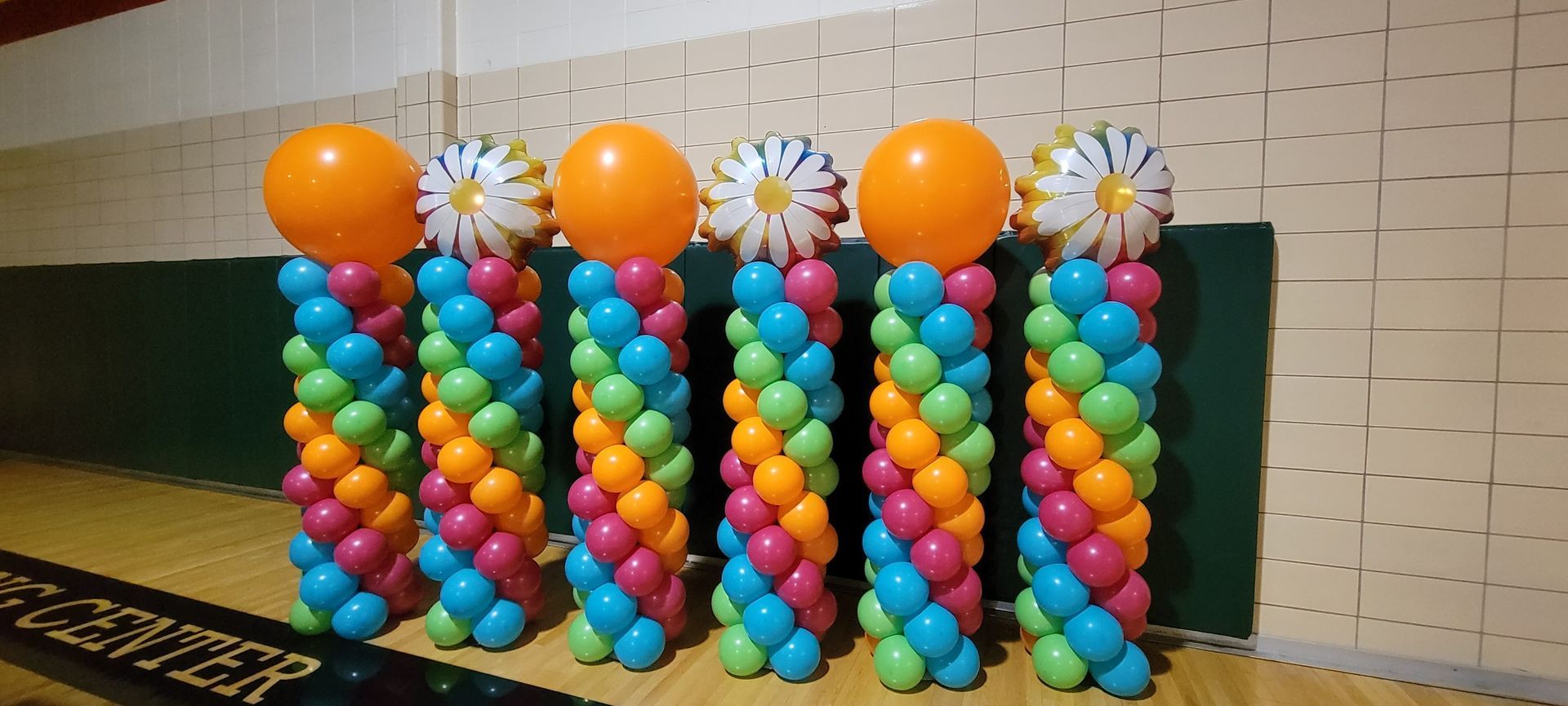A bunch of colorful balloon columns are lined up on a wooden floor