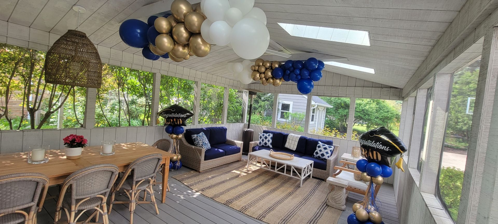 A screened in porch decorated for a graduation party with balloons hanging from the ceiling.