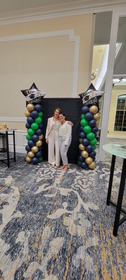 Two women are posing for a picture in front of balloons in a room.