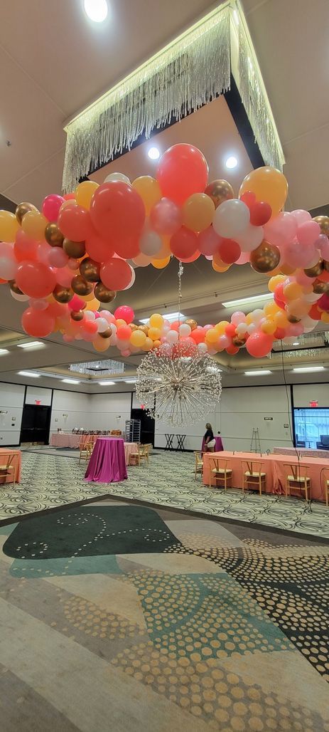 Hall with balloon arch in warm colors, tables set for event.