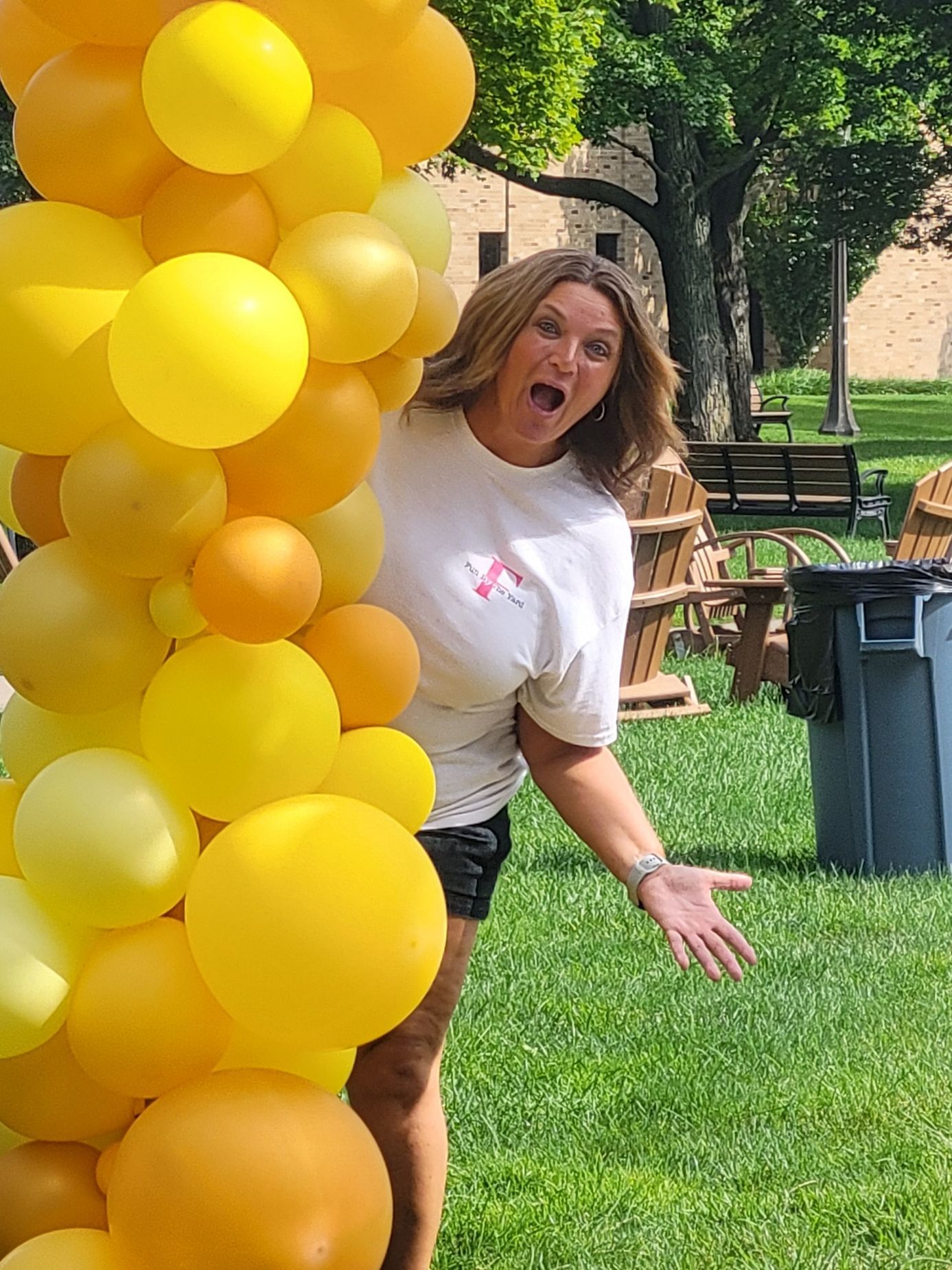 A woman is standing in front of a bunch of yellow balloons.