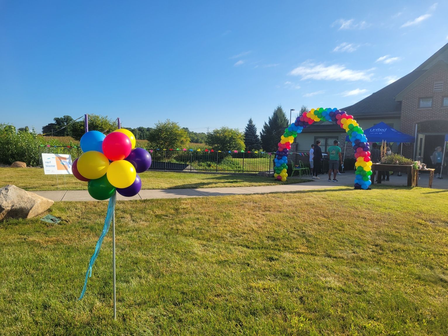 A bunch of colorful balloons are sitting in the grass in front of a house.