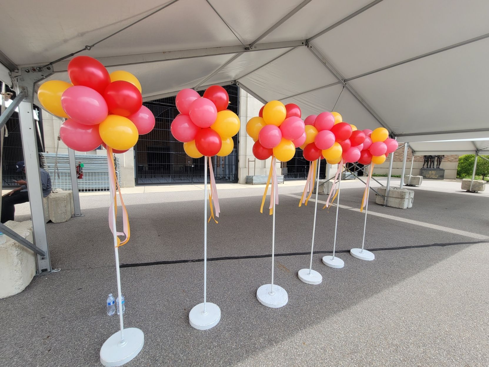 A row of red and yellow balloons on stands under a tent.