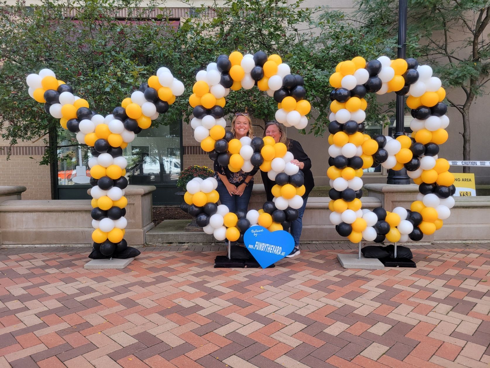 Two people are standing in front of a sign made of balloons that says YSB