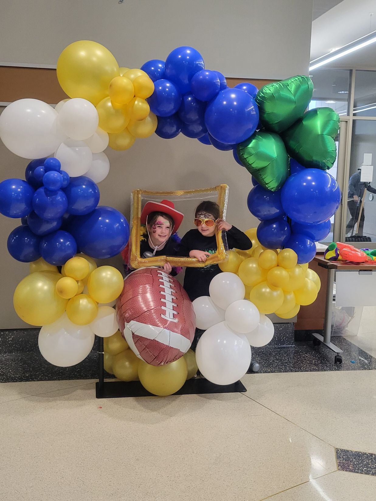 Two children are posing for a picture in front of a balloon arch.