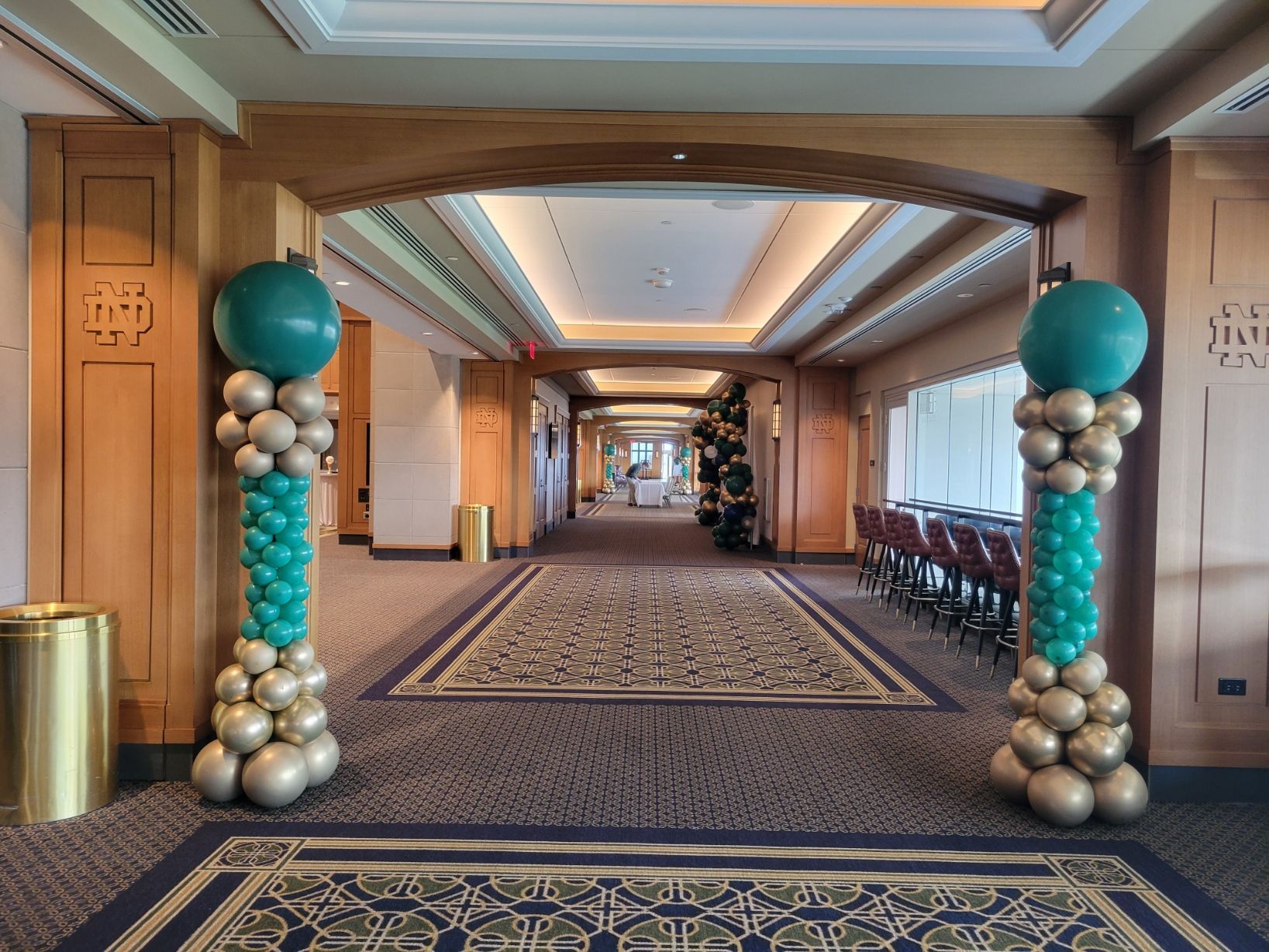 A hallway with columns decorated with green and gold balloons.