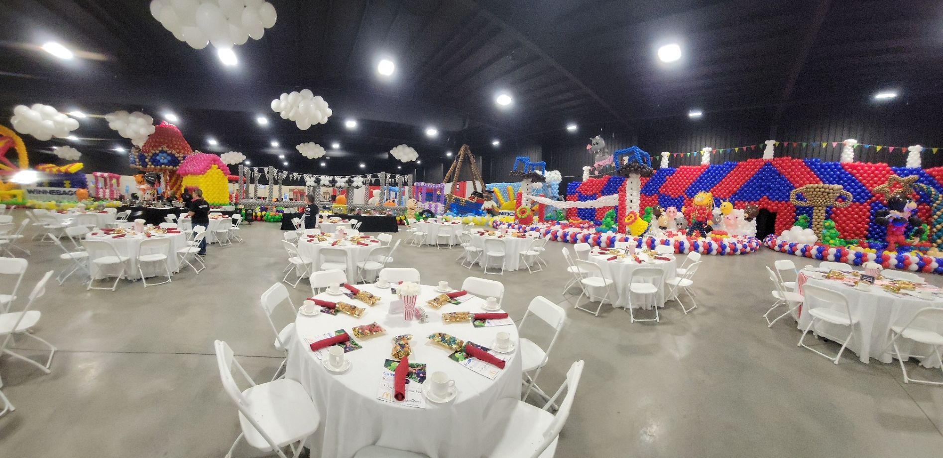 A large room filled with tables and chairs and balloons.
