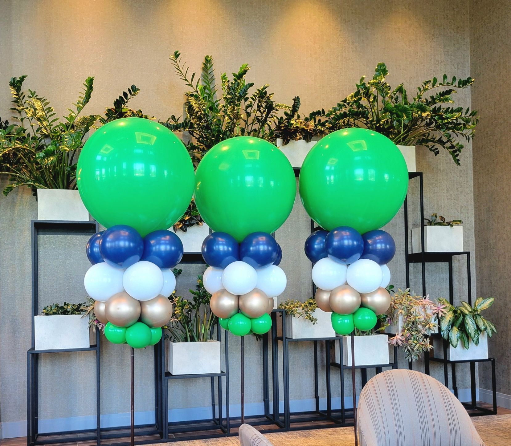 Two green balloons are surrounded by blue white and gold balloons