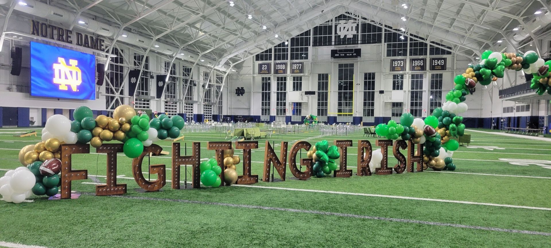 A football field decorated with green and gold balloons and wooden letters that say `` fighting irish ''.