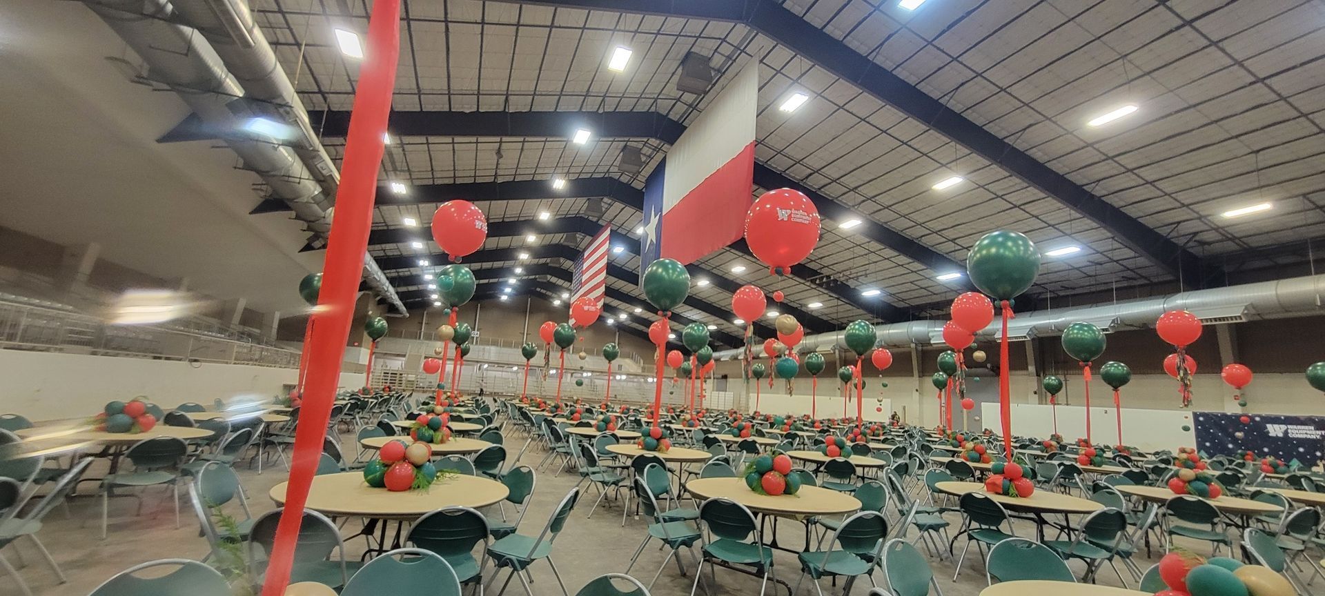 A large room with tables and chairs decorated with balloons and a flag.