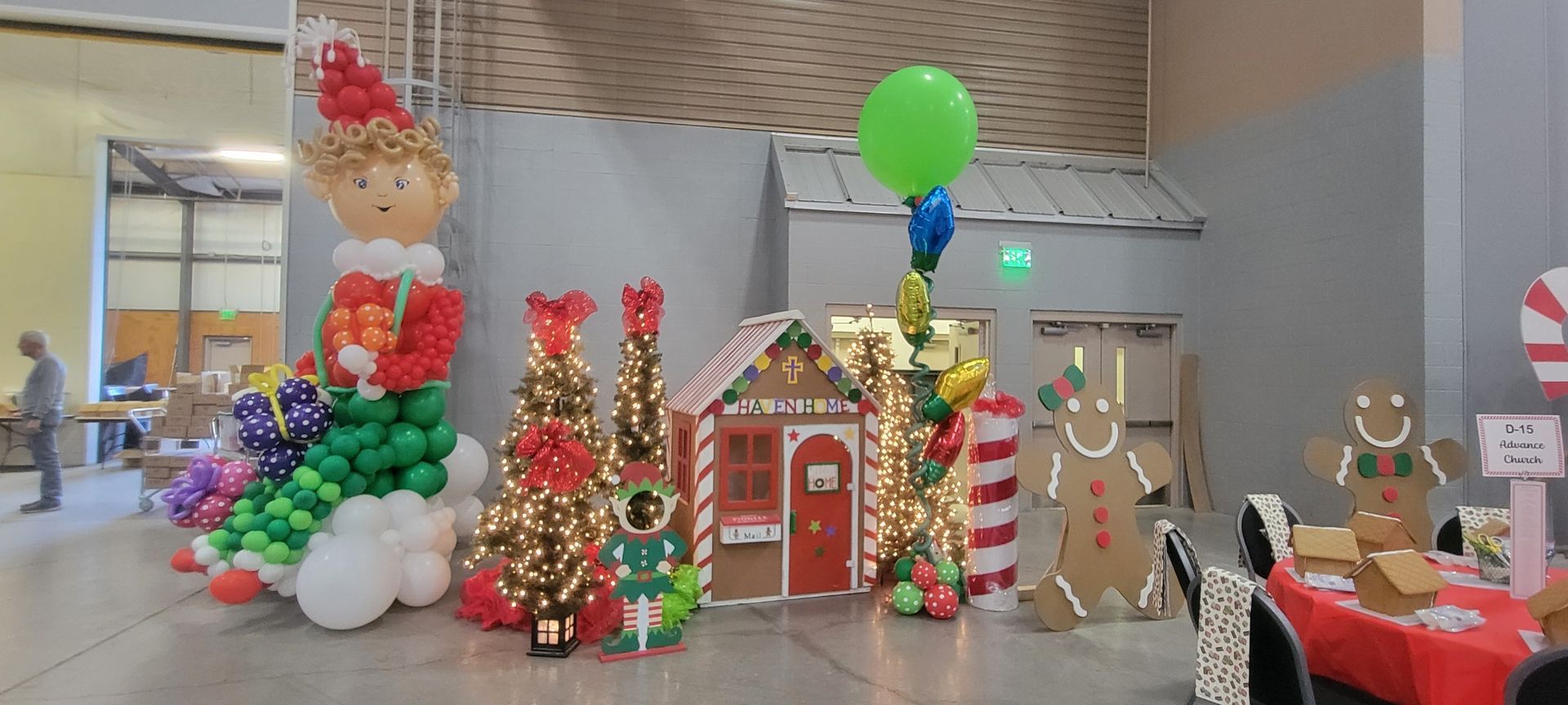 A room decorated for christmas with balloons , gingerbread men , trees and a gingerbread house.