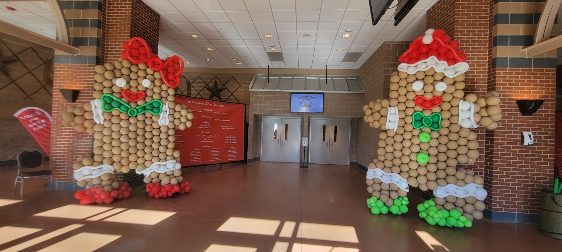 Two gingerbread men made out of balloons are standing in a hallway.