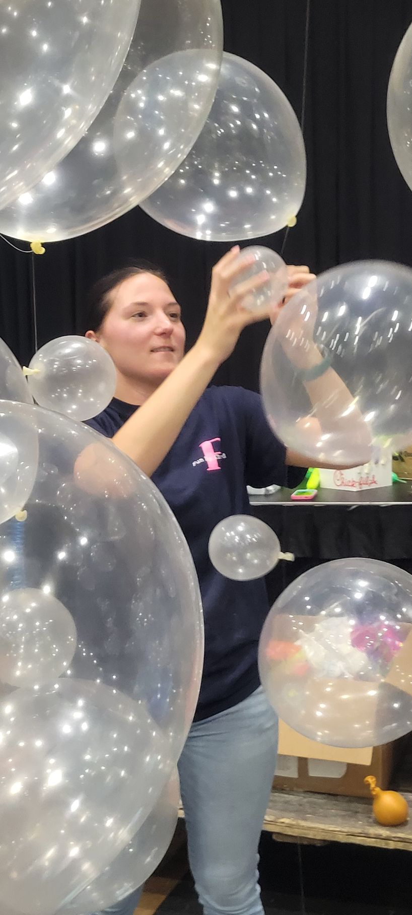 Woman amid clear balloons, reaching up to touch one, indoors.