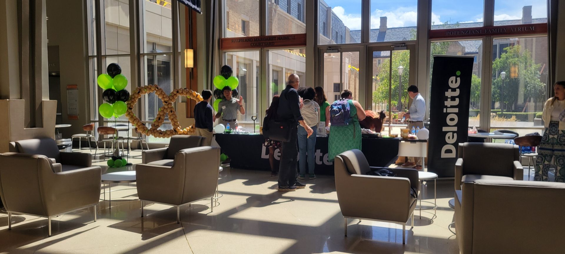People at a Deloitte recruitment event, tables set up, balloons, and an oversized pretzel.