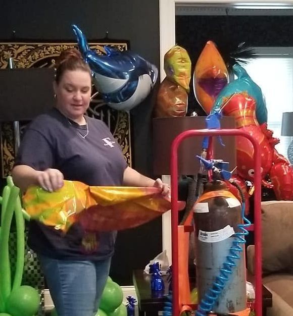 A woman is standing in front of a cart full of balloons for helium inflation