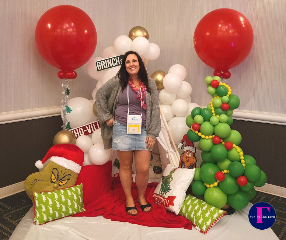 A woman is standing in front of a christmas tree made of balloons.