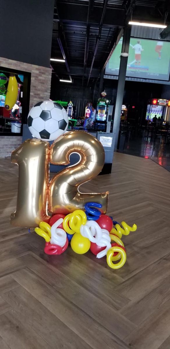 A bunch ofbirthday balloons are sitting on a wooden floor in a room. Soccer. Balloon Marquee.
