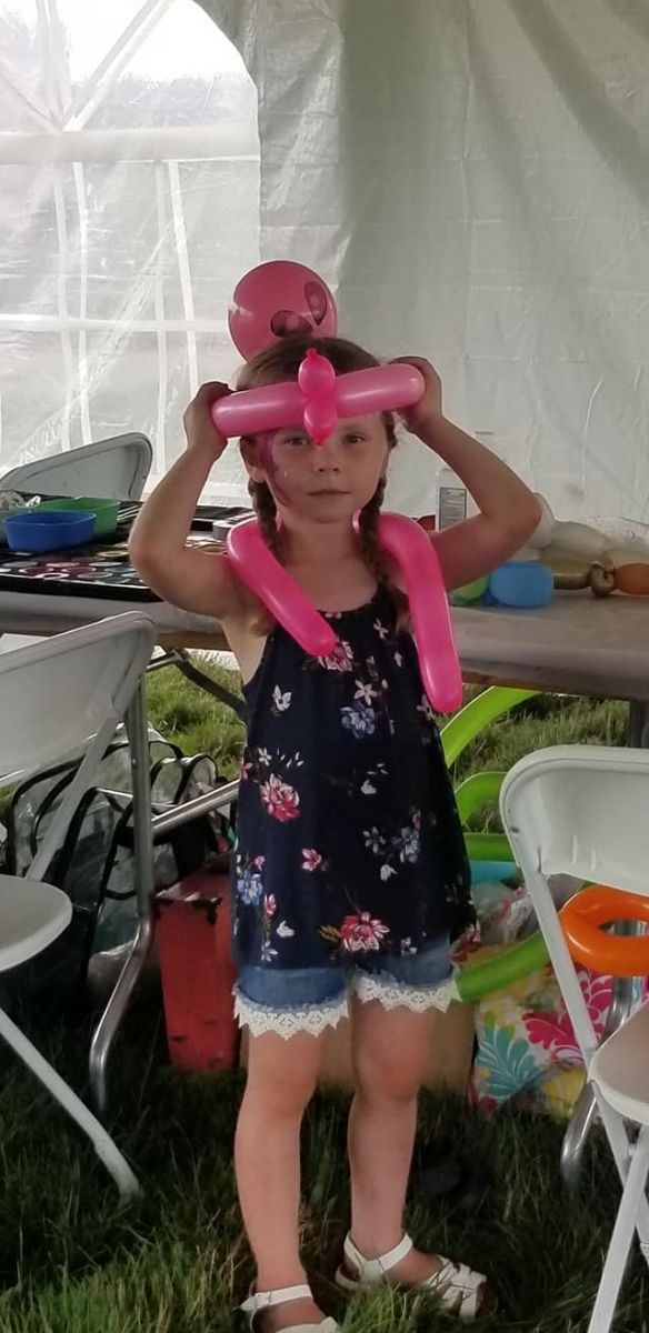 A little girl is standing in the grass with balloons on her head.