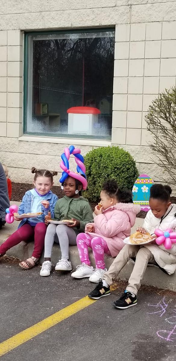 A group of children are sitting on the sidewalk eating pizza. Balloon Twisting Entertainment