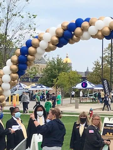 A group of people are standing under a blue and gold balloon arch.