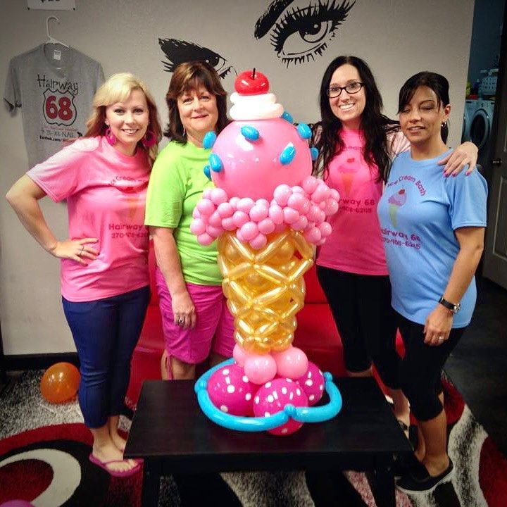 Four women pose with a large balloon ice cream cone on a table.