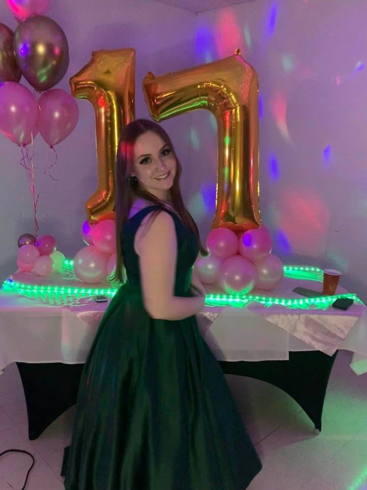 A woman in a green dress is standing in front of a table with balloons and a number 11 balloon.