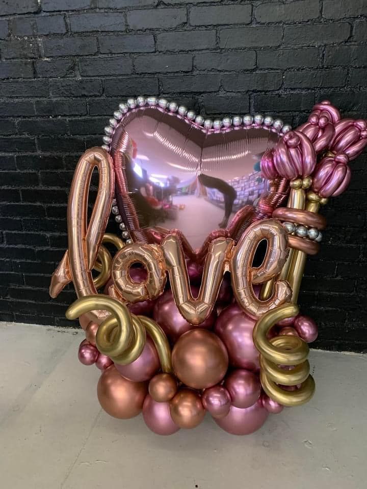 A heart shaped balloon with the word love written on it is surrounded by other balloons.