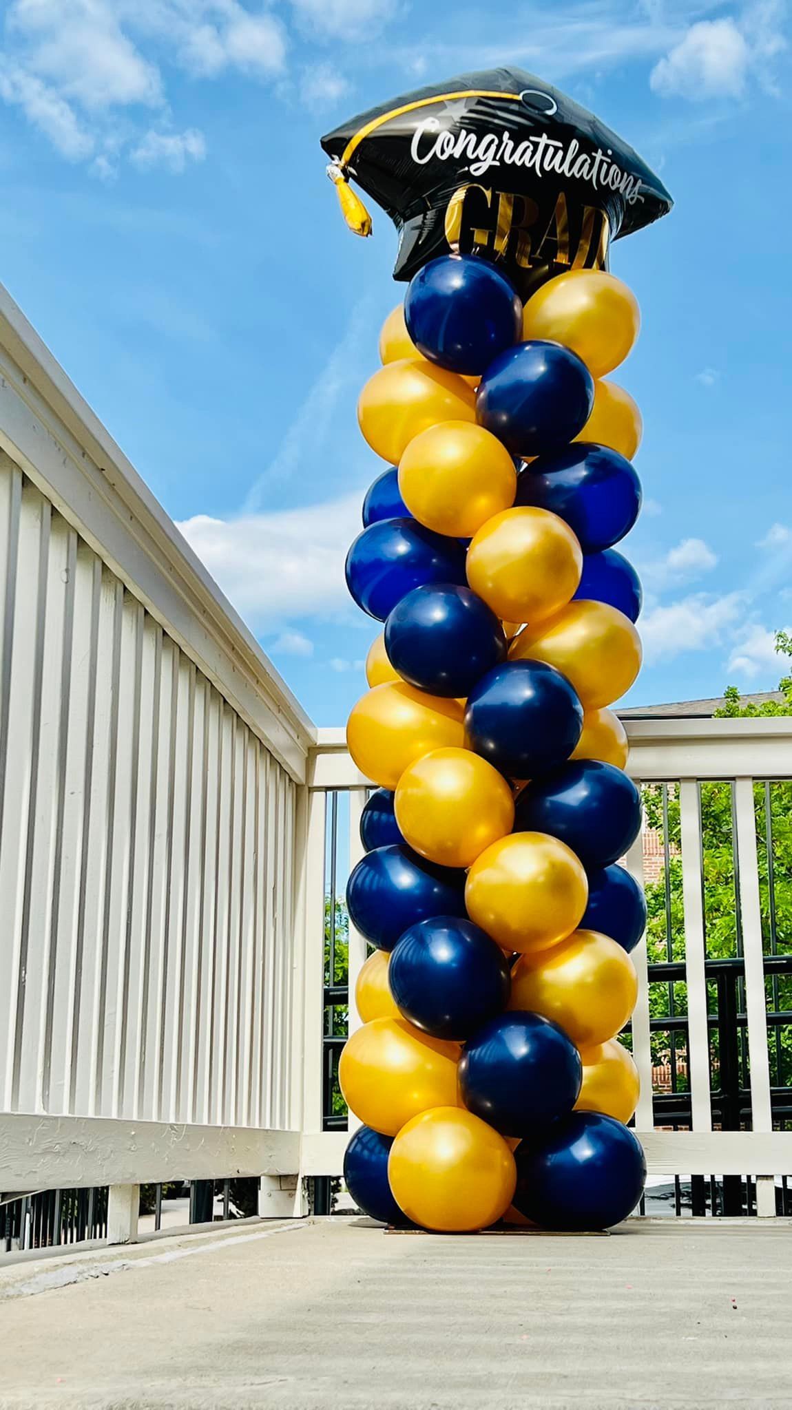 A tower of blue and gold balloons with a graduation cap on top.