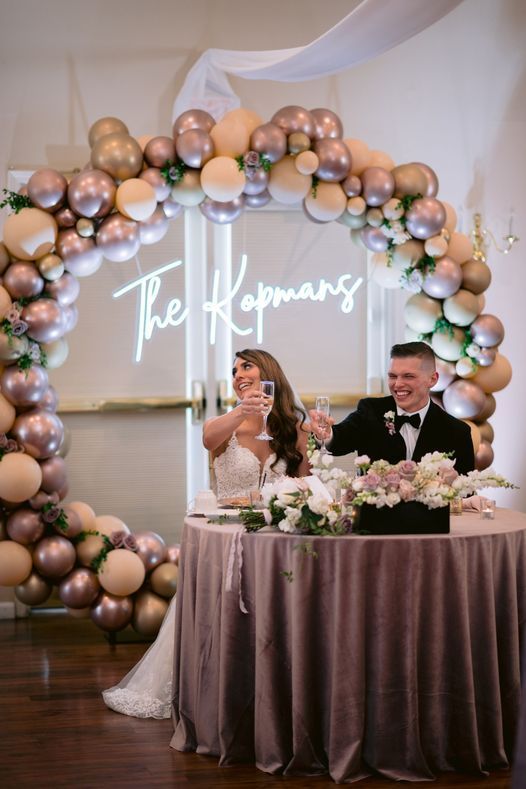 A bride and groom are sitting at a table with balloons in the background.