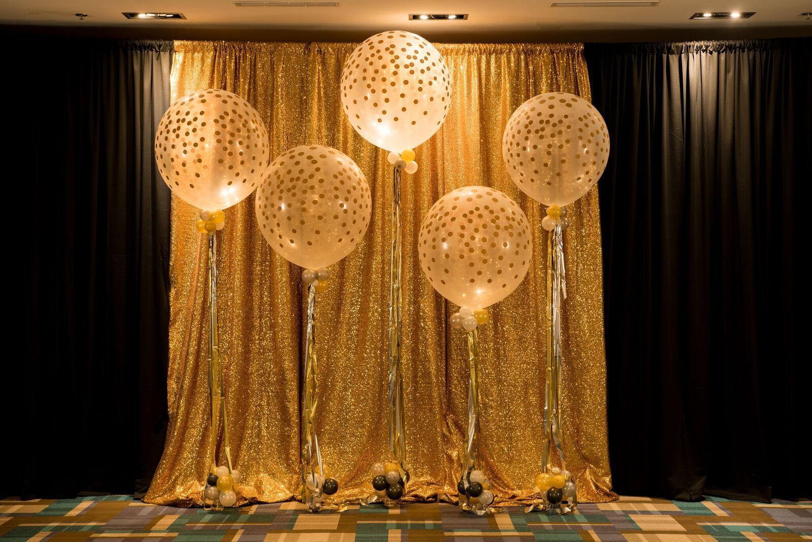 Jumbo helium confetti filled balloons sitting in front of a gold curtain.