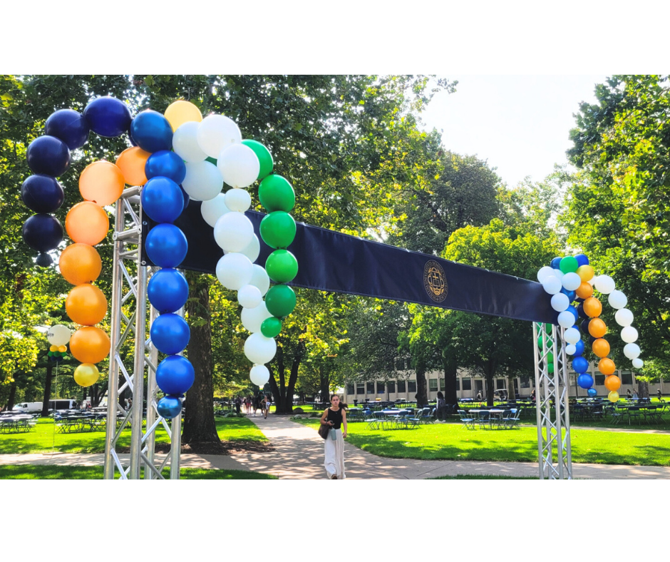A woman stands under a balloon arch in a park