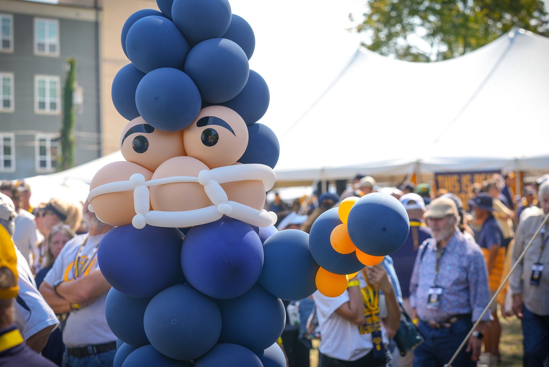 Balloon sculpture of a person in blue and tan, surrounded by people and tents outdoors.